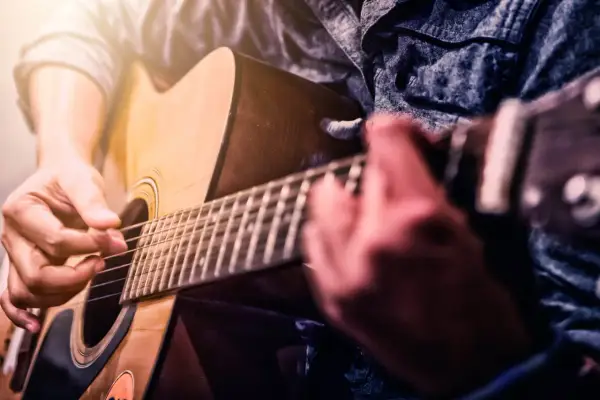 Dłonie grające na gitarze akustycznej. Czy gra na gitarze jest trudna? Zależy od determinacji i praktyki.